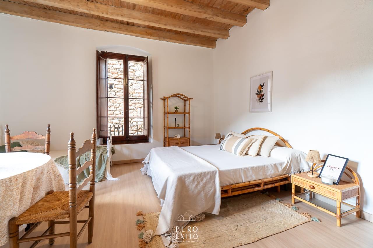 A large bedroom with a double bed, a single bed and a table, under a heavy beamed ceiling.