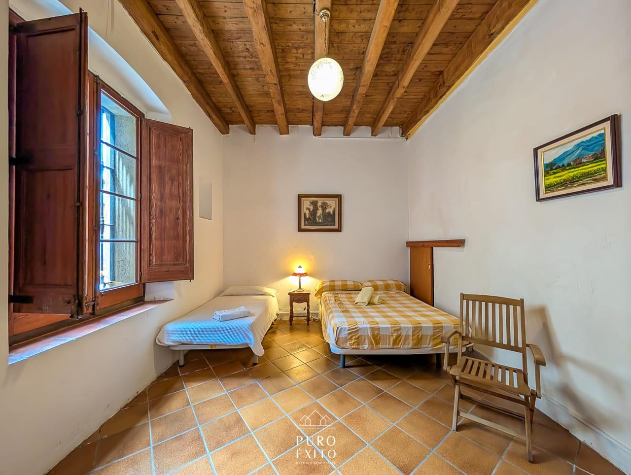 A bedroom containing both a double bed and a single bed, with terracotta floor tiles and a shuttered window.