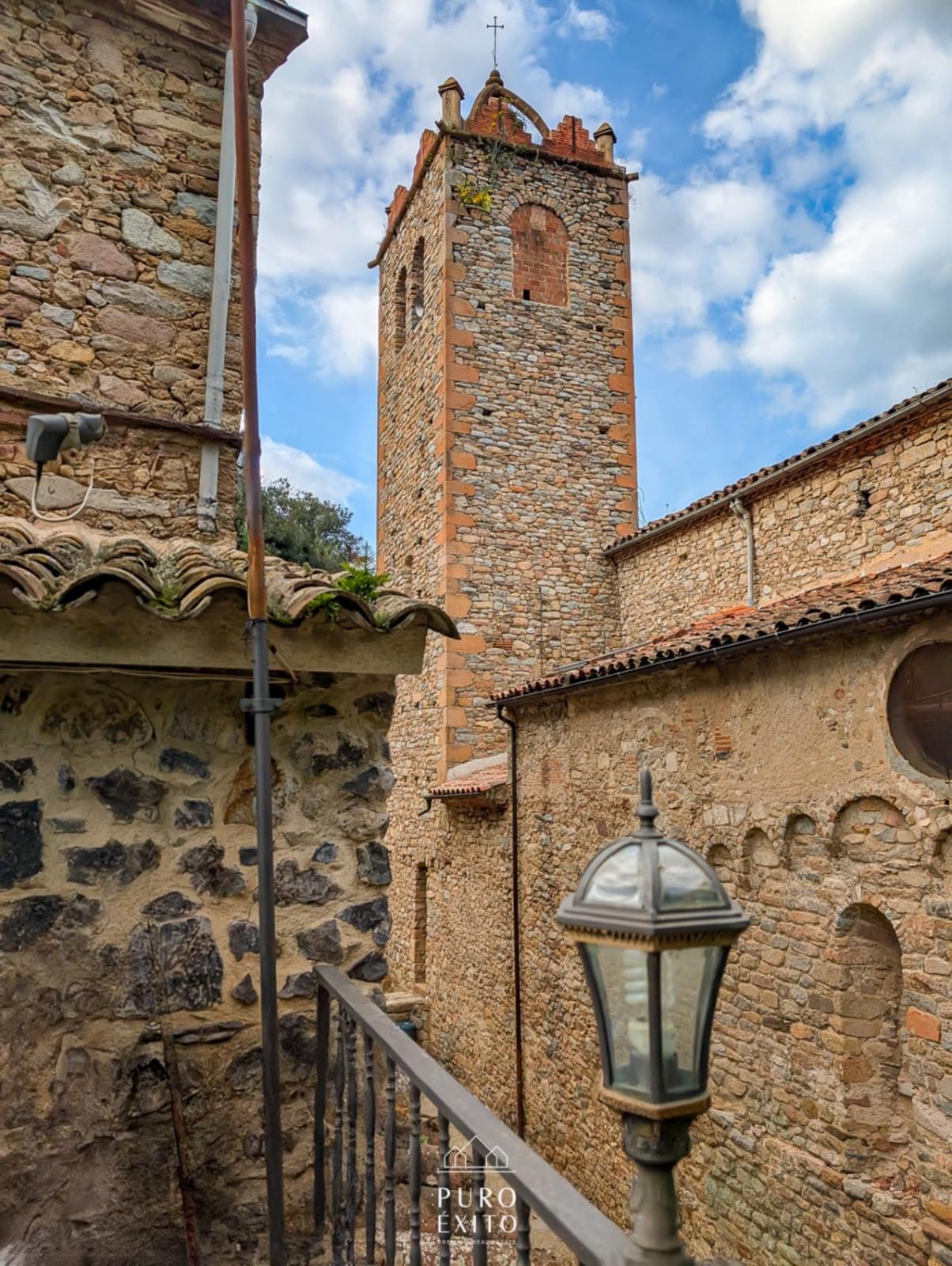 The stone bell tower of Osor's church rising above the rooftops, seen from a narrow lane beside the house.