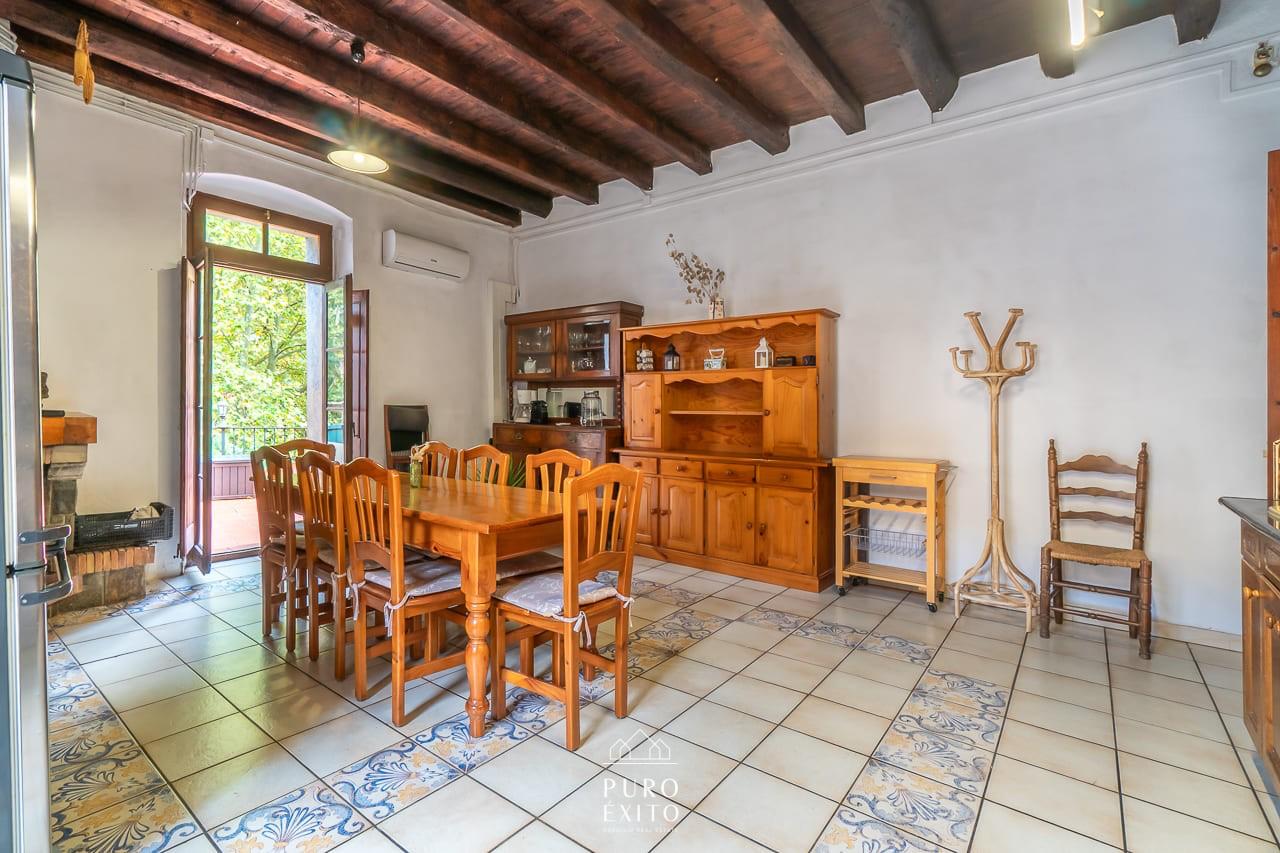 The dining room: a long wooden table under a beamed ceiling, with balcony doors open onto the trees outside.