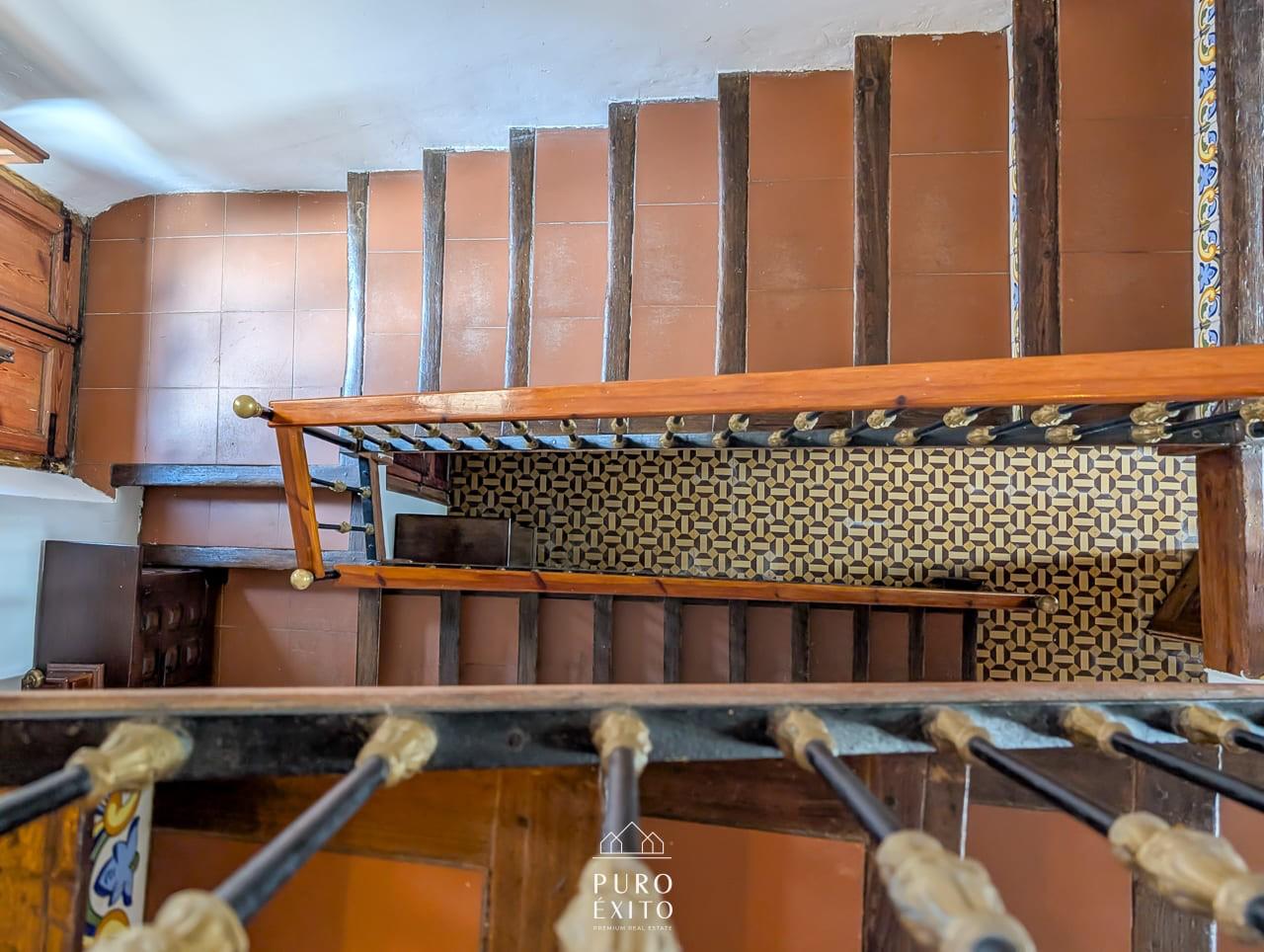 Looking down the stairwell: terracotta treads, painted tile risers and a turned wooden handrail.