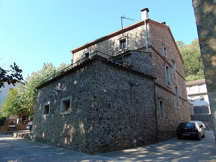 A stone house in Osor with a first-floor terrace and iron railings, wooded hillside rising behind.